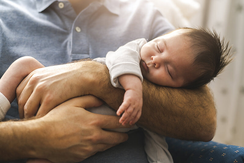 Baby boy sleep in the father hand sit on chair one the bedroom