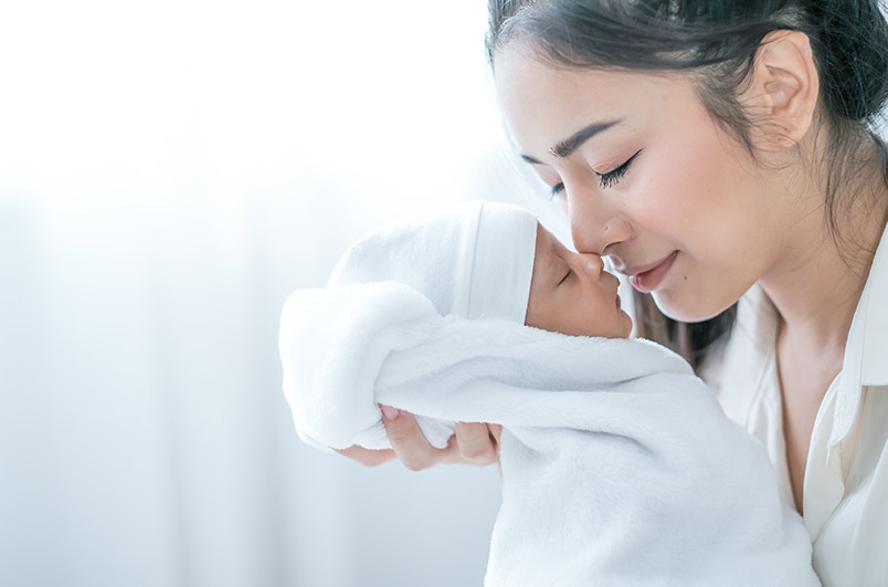 Beautiful Asian mother look like Indian mom nose touching at newborn baby nose in bedroom in front of glass windows with white curtain with concept love attractive and family bonding.
